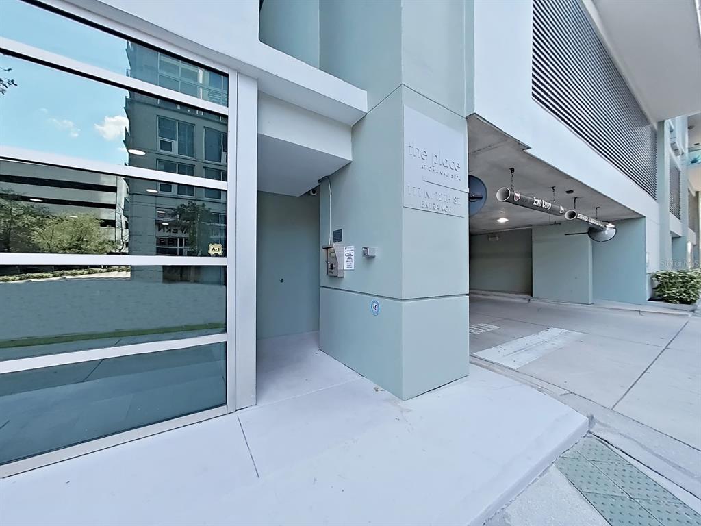 The exterior entrance to a modern apartment building features a glass door and parking garage — 111 N 12TH STREET UNIT 1810, TAMPA, FL