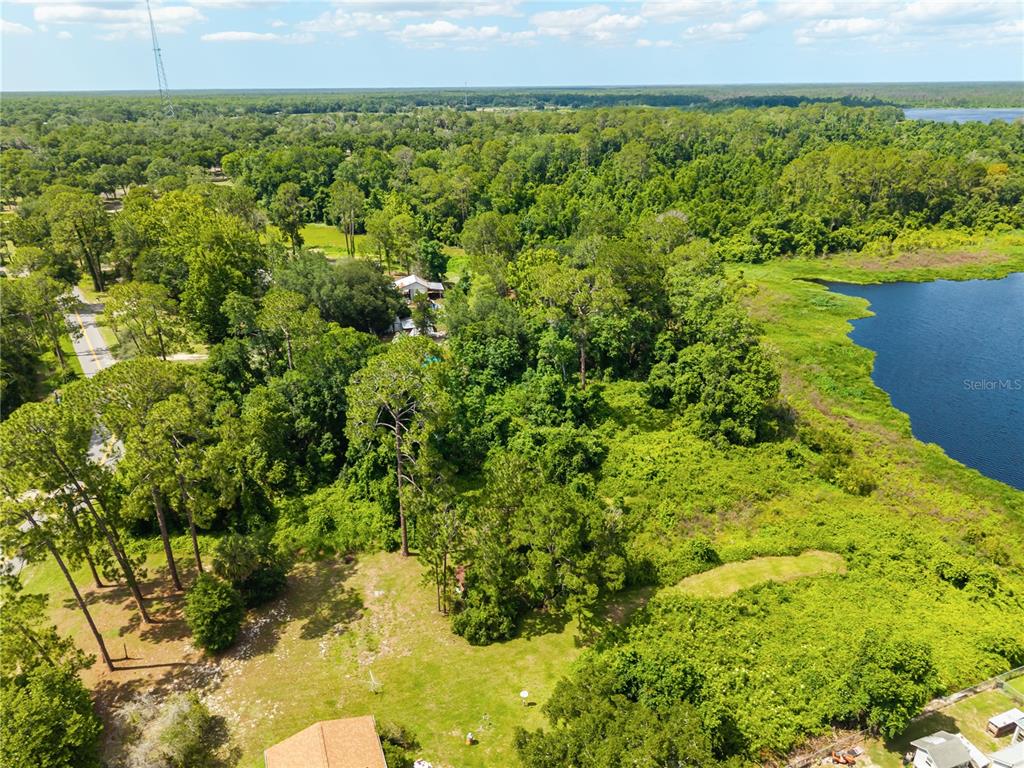 An aerial view shows a wooded lot with a house next to a large lake — FISHERMANS ROAD, PAISLEY, FL