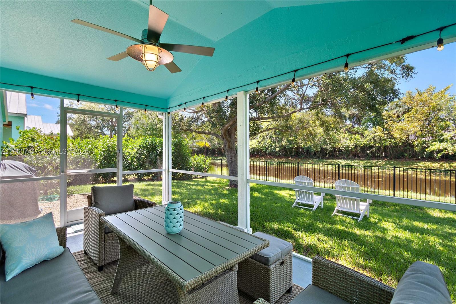A screened-in patio features a turquoise ceiling, a ceiling fan, and outdoor furniture overlooking a canal — 104 Old Jupiter Beach Road, Jupiter FL 33477, JUPITER, FL