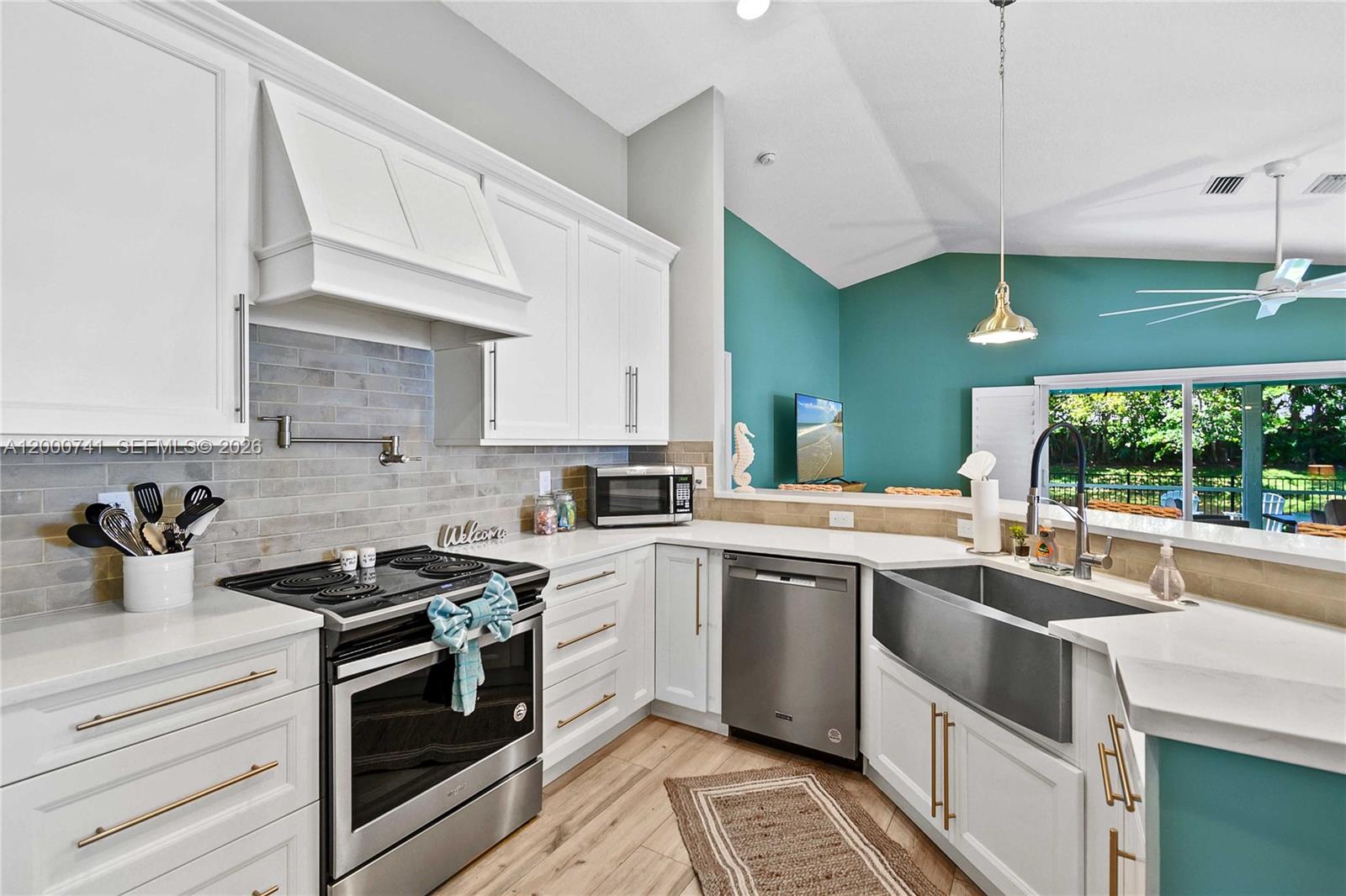 A modern kitchen features white cabinets, stainless steel appliances, a farmhouse sink, and teal walls — 104 Old Jupiter Beach Road, Jupiter FL 33477, JUPITER, FL