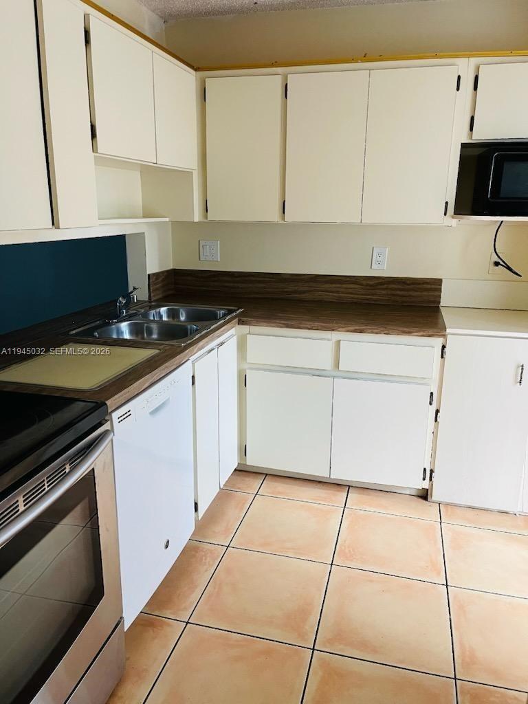 A kitchen features white cabinets, a wood-look laminate countertop, and light-colored floor tiles — 842 Banks Rd, Coconut Creek FL 33063, COCONUT CREEK, FL