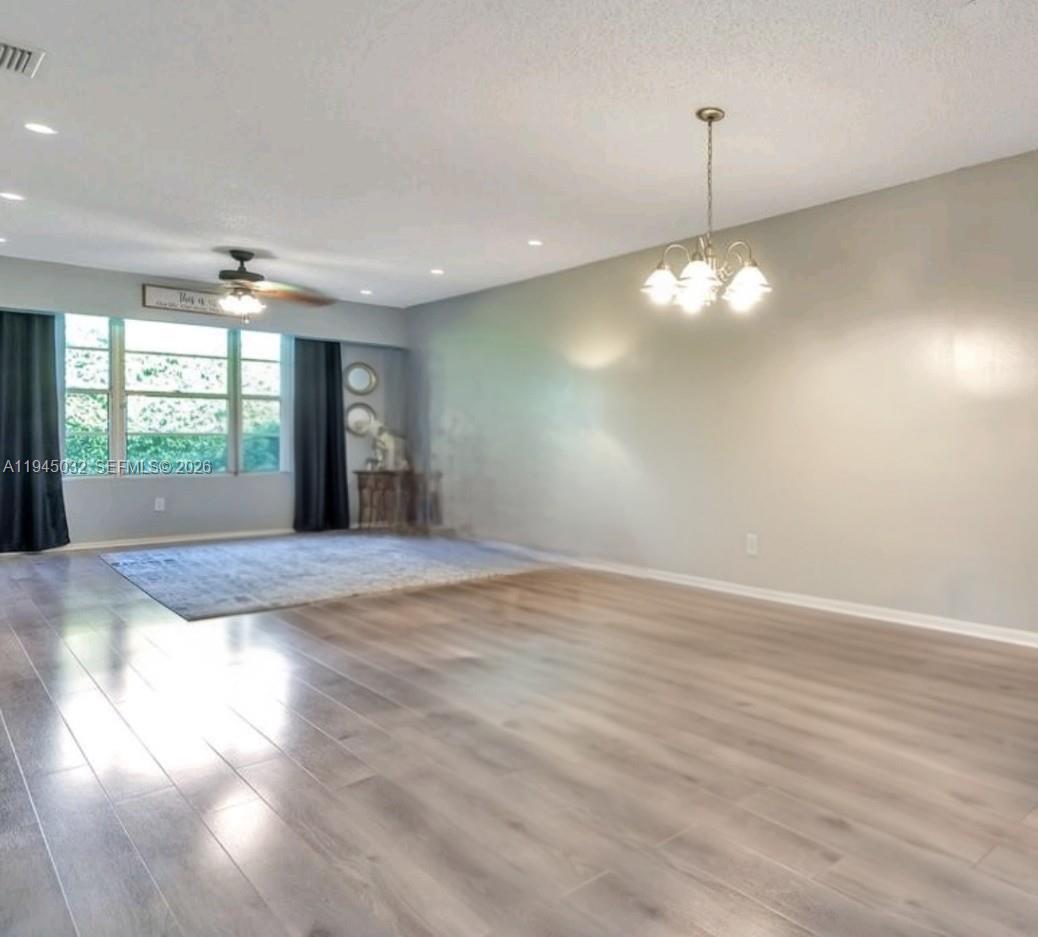 A spacious living room features light wood-look flooring, a ceiling fan, and a dining chandelier — 842 Banks Rd, Coconut Creek FL 33063, COCONUT CREEK, FL