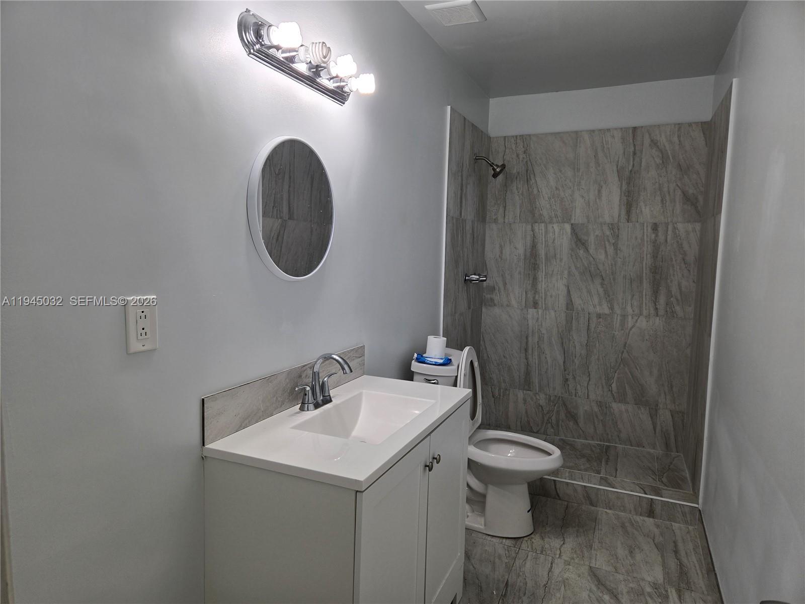 A bathroom features a white vanity, a round mirror, and a tiled walk-in shower — 842 Banks Rd, Coconut Creek FL 33063, COCONUT CREEK, FL