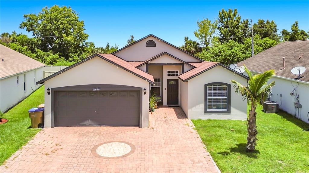 A single-story house with a brick driveway, a two-car garage, and a palm tree — 2469 HYBRID DRIVE, KISSIMMEE, FL