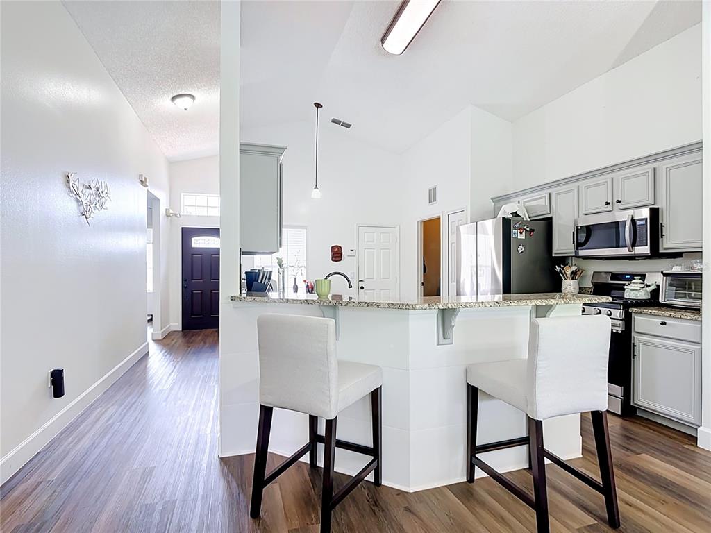 A kitchen features a granite-topped breakfast bar with two stools and light gray cabinetry — 2469 HYBRID DRIVE, KISSIMMEE, FL