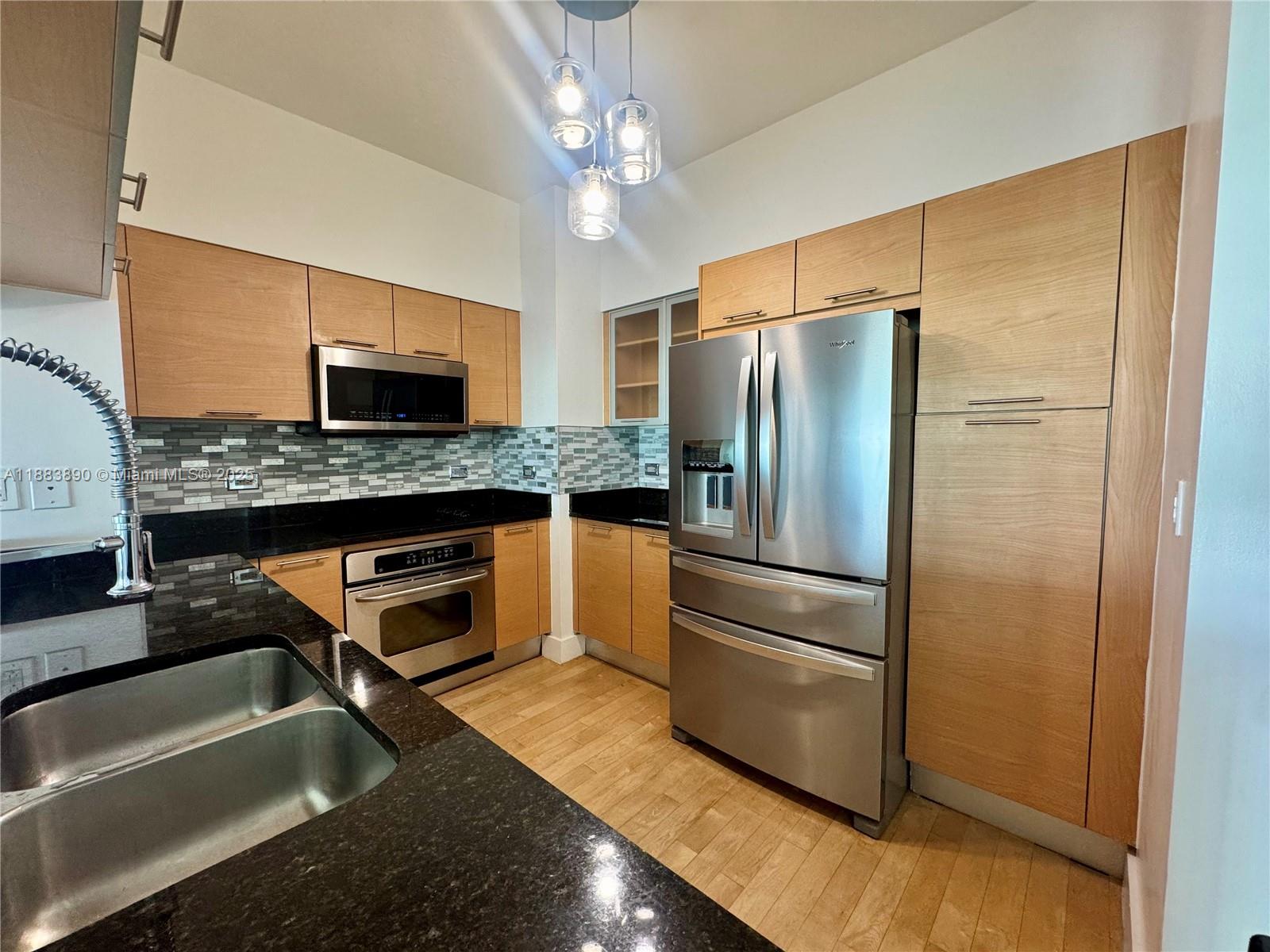 A kitchen features light wood cabinets, black granite countertops, stainless steel appliances, and pendant lighting — 31 SE 5th St # 3817, Miami FL 33131, MIAMI, FL
