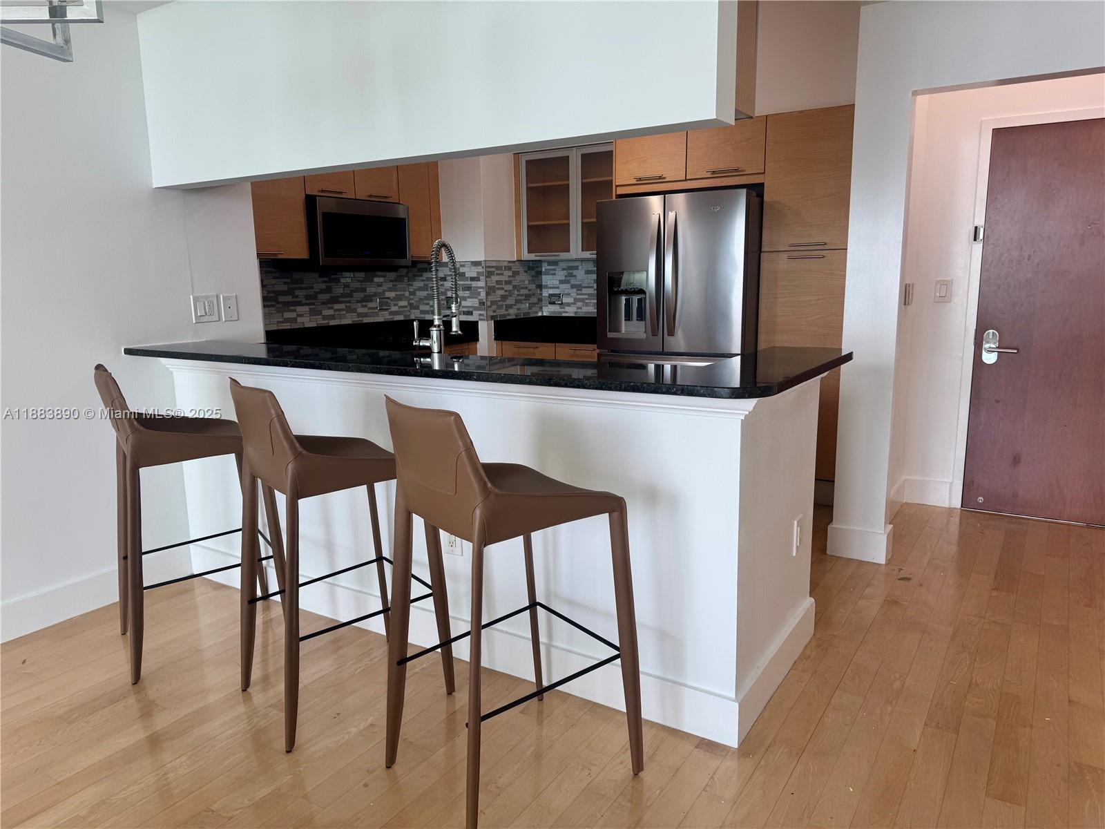 A kitchen features a black countertop, brown bar stools, and light wood cabinetry — 31 SE 5th St # 3817, Miami FL 33131, MIAMI, FL