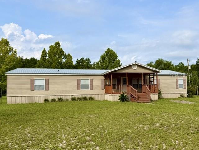 A single-story manufactured home with tan siding, a metal roof, and a front porch — 4689 NW 26TH STREET, BELL, FL