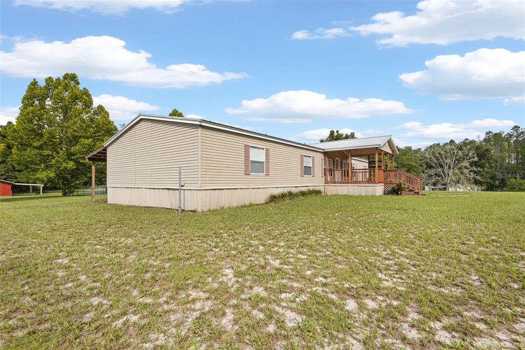 A tan manufactured home with a covered wooden porch sits on a grassy lot — 4689 NW 26TH STREET, BELL, FL