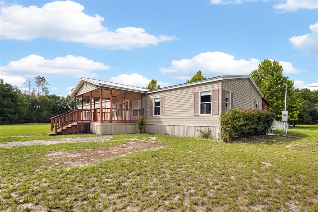 A tan manufactured home with a wooden porch sits on a grassy lot under a sky — 4689 NW 26TH STREET, BELL, FL