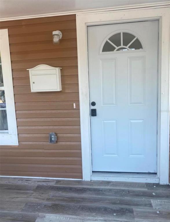 A white front door with a half-moon window sits beside a mailbox on brown siding — 1810 N BRACK STREET, KISSIMMEE, FL
