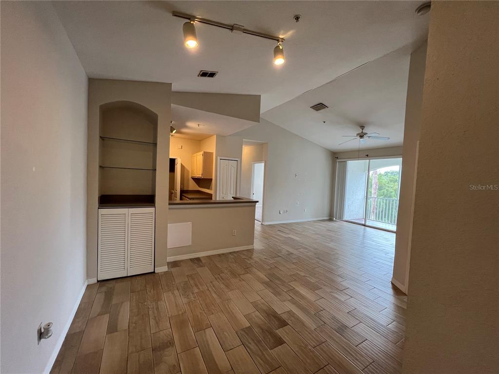 An open-concept living area features wood-look tile flooring, a built-in shelving unit, and a balcony — 2537 MAITLAND CROSSING WAY UNIT 308, ORLANDO, FL