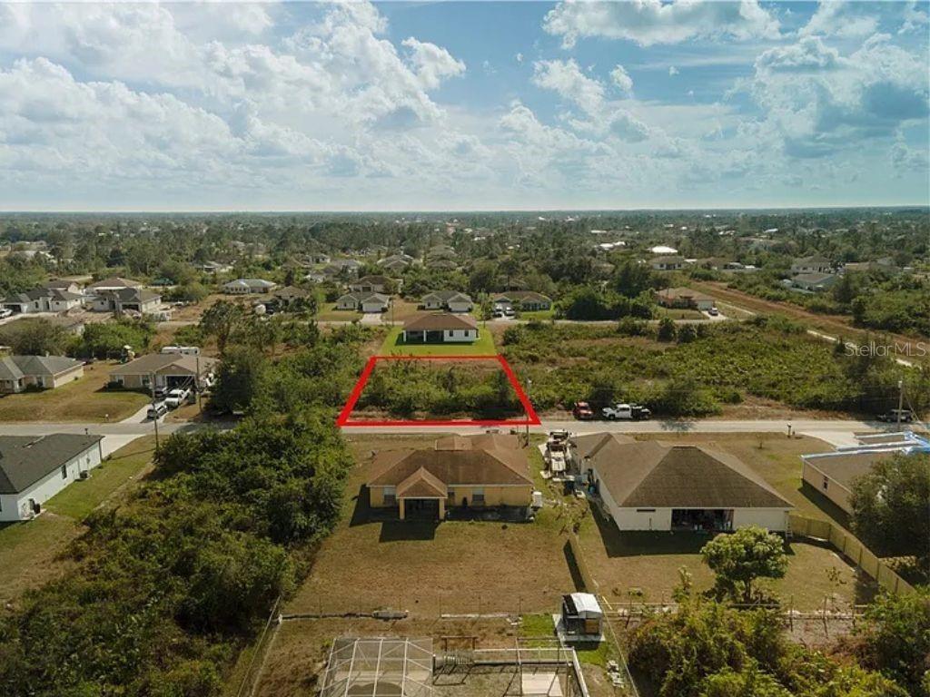 An aerial view shows a vacant, rectangular residential lot outlined in red along a paved road — 2613 3RD STREET SW, LEHIGH ACRES, FL