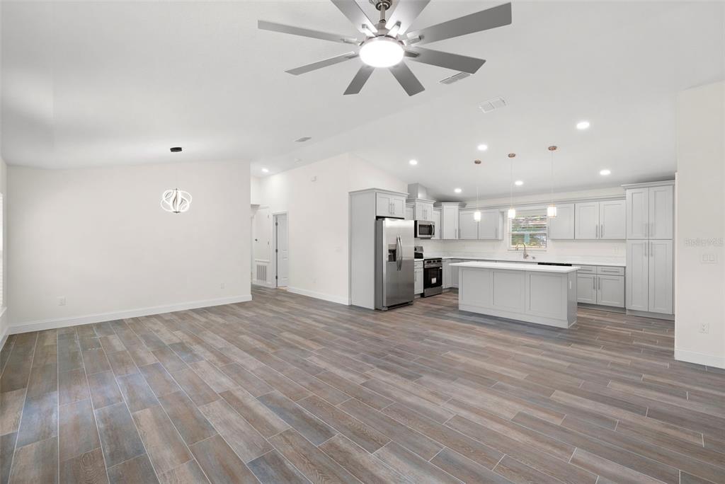 An open-concept kitchen and living area featuring light gray cabinetry, an island, and wood-look flooring — 5062 80TH LANE N, ST PETERSBURG, FL