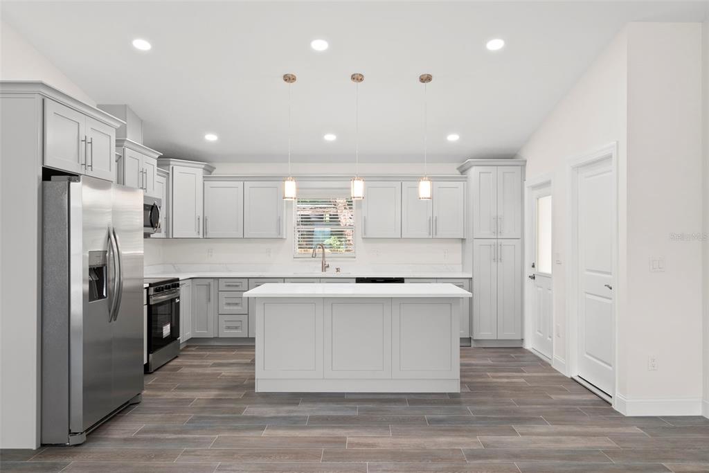 A modern kitchen features light gray cabinets, a central island, and wood-look tile flooring — 5062 80TH LANE N, ST PETERSBURG, FL