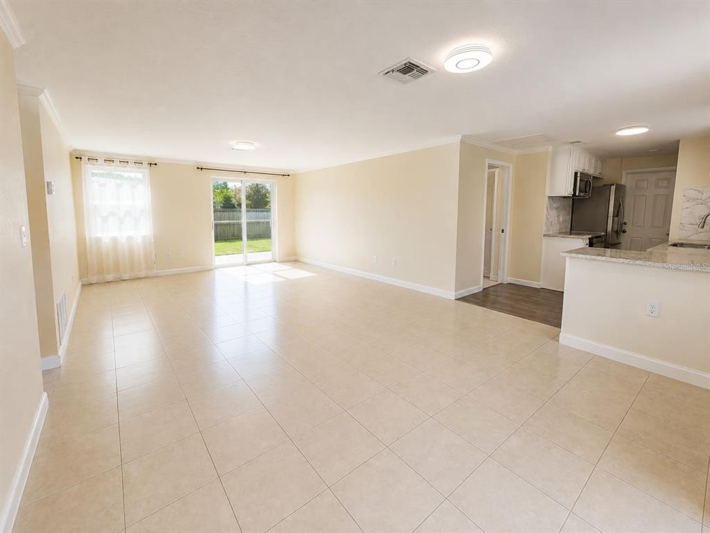 An open-concept living area features light-colored tile flooring, beige walls, and a sliding glass door — 14490 SW 41ST AVENUE ROAD, OCALA, FL
