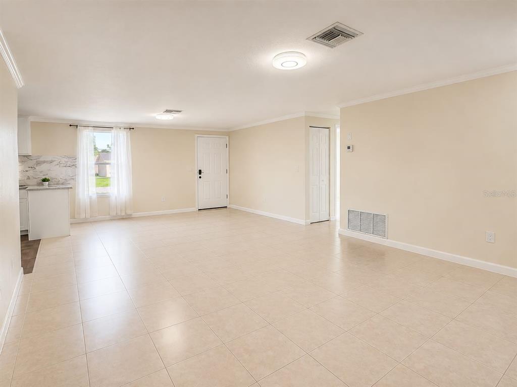 A spacious, light-colored room with tiled floors, a white door, and an open kitchen area — 14490 SW 41ST AVENUE ROAD, OCALA, FL