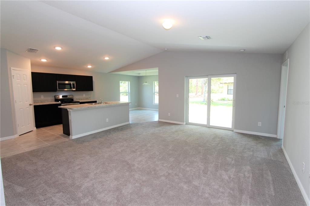 A living room with gray carpet opens to a kitchen with dark cabinets and counters — 154 AUSTRALIAN DRIVE, ROTONDA WEST, FL