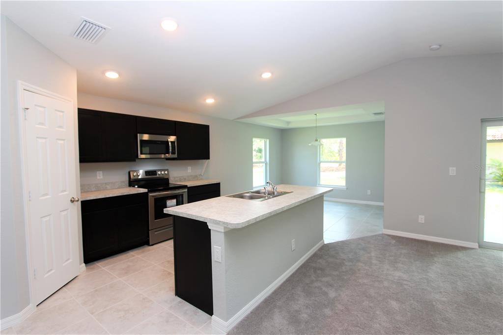 A kitchen features dark cabinets, stainless steel appliances, a center island, and tile flooring — 154 AUSTRALIAN DRIVE, ROTONDA WEST, FL