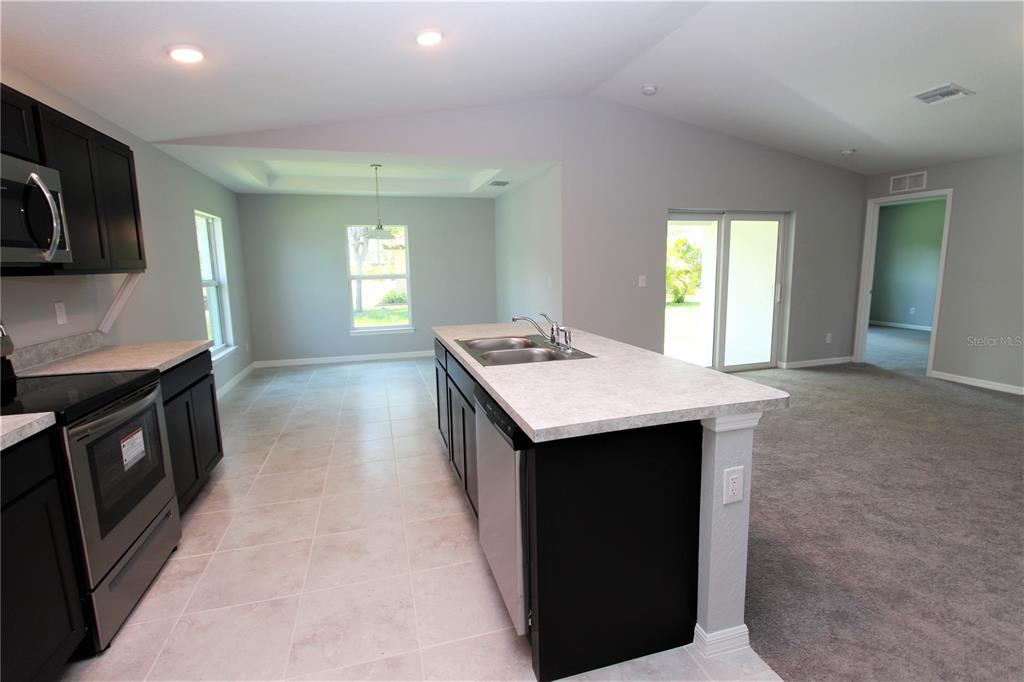 A kitchen with dark cabinets, a central island with a sink, and light-colored flooring — 154 AUSTRALIAN DRIVE, ROTONDA WEST, FL