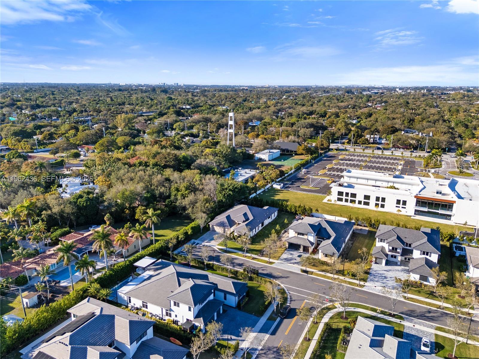 An aerial view shows a suburban neighborhood with modern houses, a large parking lot, and dense trees — 7387 SW 74th Ln, Miami FL 33143, MIAMI, FL