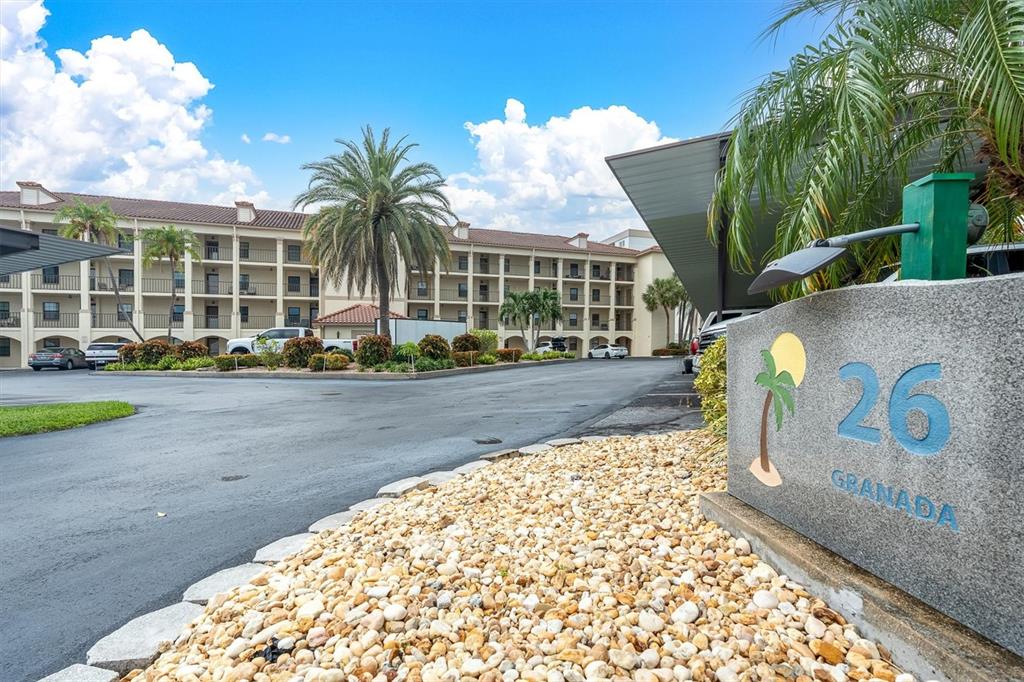 A stone sign labeled 26 Granada stands in front of a multi-story apartment building — 19029 US HIGHWAY 19 N UNIT 26-208, CLEARWATER, FL