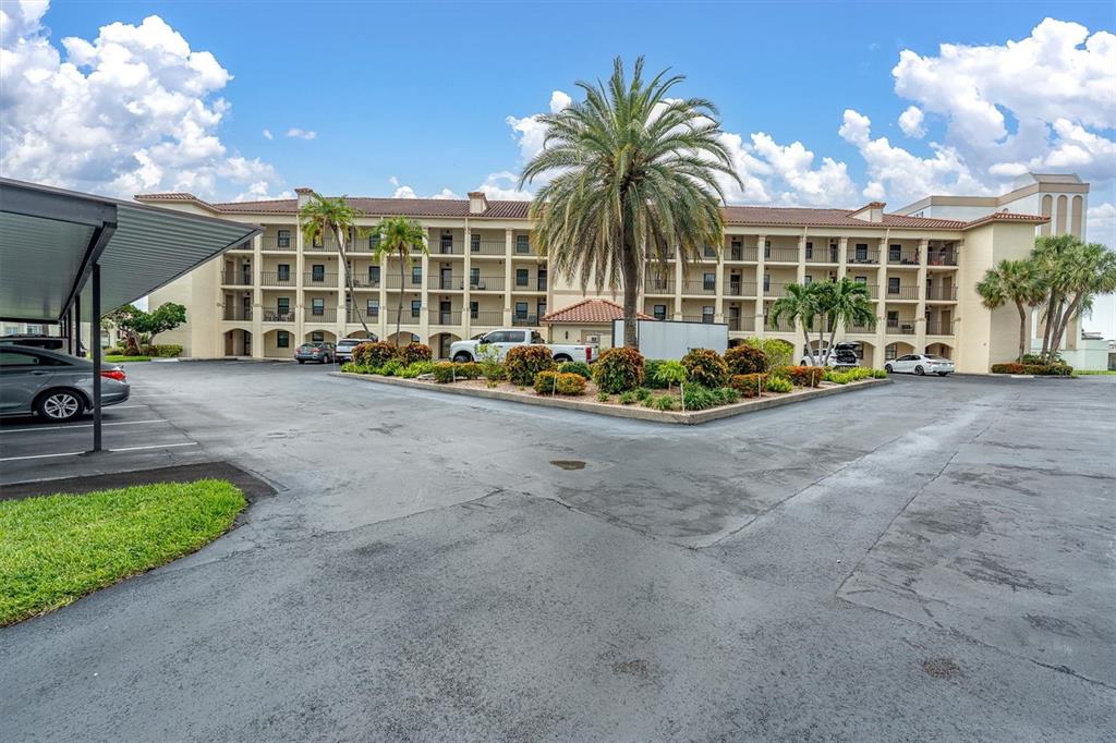 A multi-story apartment building with a parking lot and palm trees under a blue sky — 19029 US HIGHWAY 19 N UNIT 26-208, CLEARWATER, FL