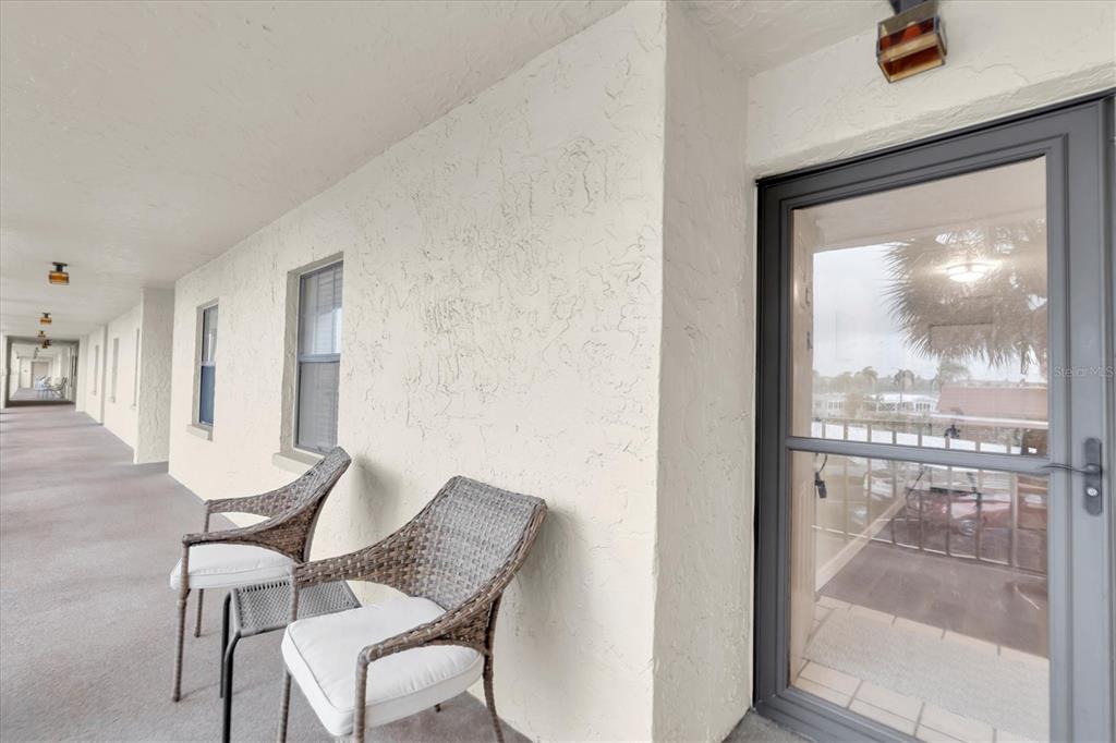 Two wicker chairs sit on a covered outdoor walkway outside a glass door — 19029 US HIGHWAY 19 N UNIT 26-208, CLEARWATER, FL