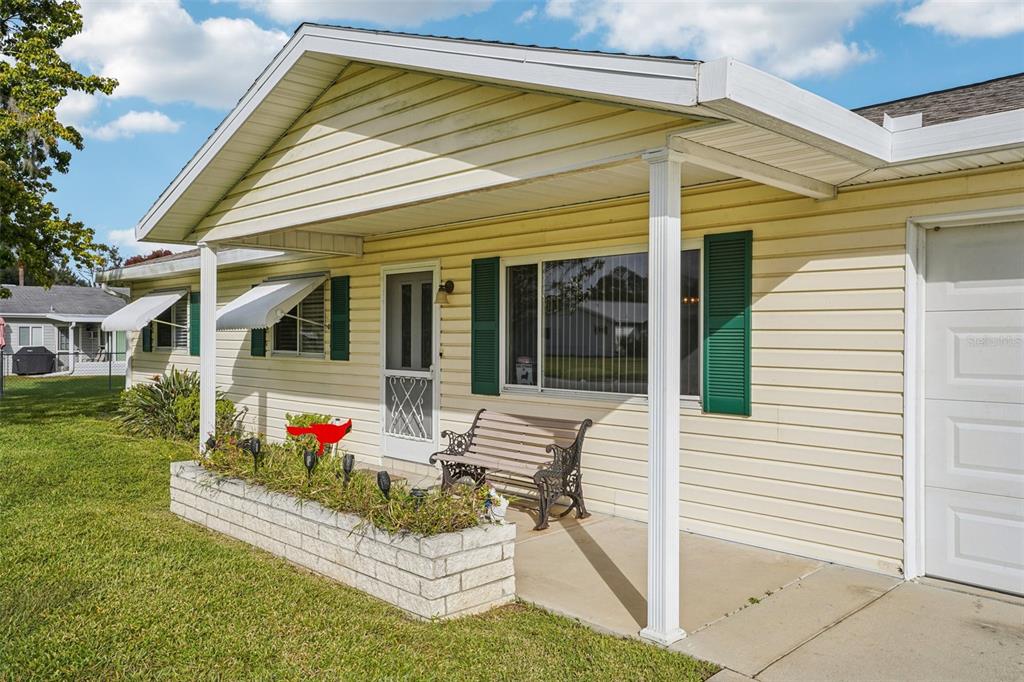 A yellow-sided house features a covered front porch with a brick planter and a bench — 10339 SE 179TH STREET, SUMMERFIELD, FL