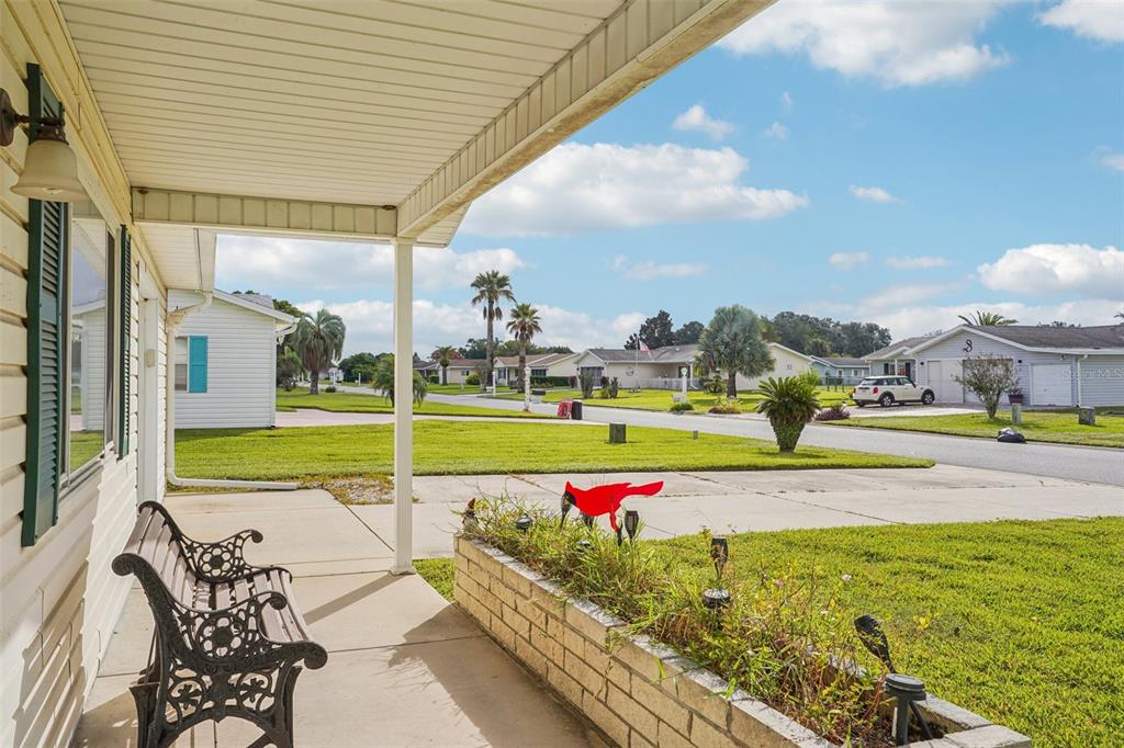A covered front porch with a metal bench overlooks a suburban street and grassy lawn — 10339 SE 179TH STREET, SUMMERFIELD, FL