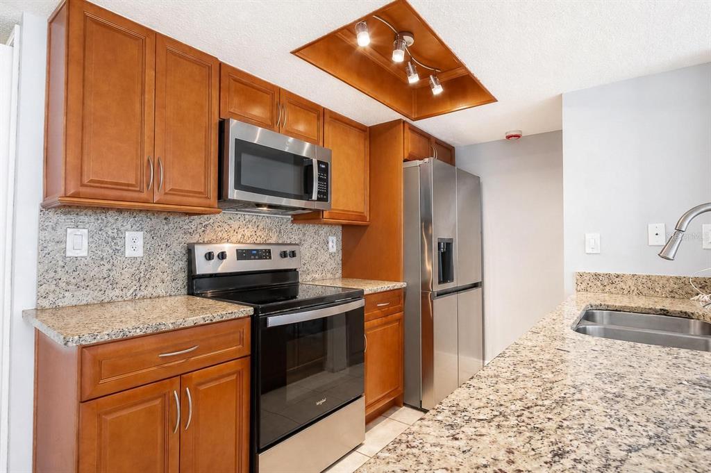 A kitchen with wood cabinets, granite countertops, stainless steel appliances, and a recessed ceiling light — 2739 N POINCIANA BOULEVARD UNIT 79, KISSIMMEE, FL