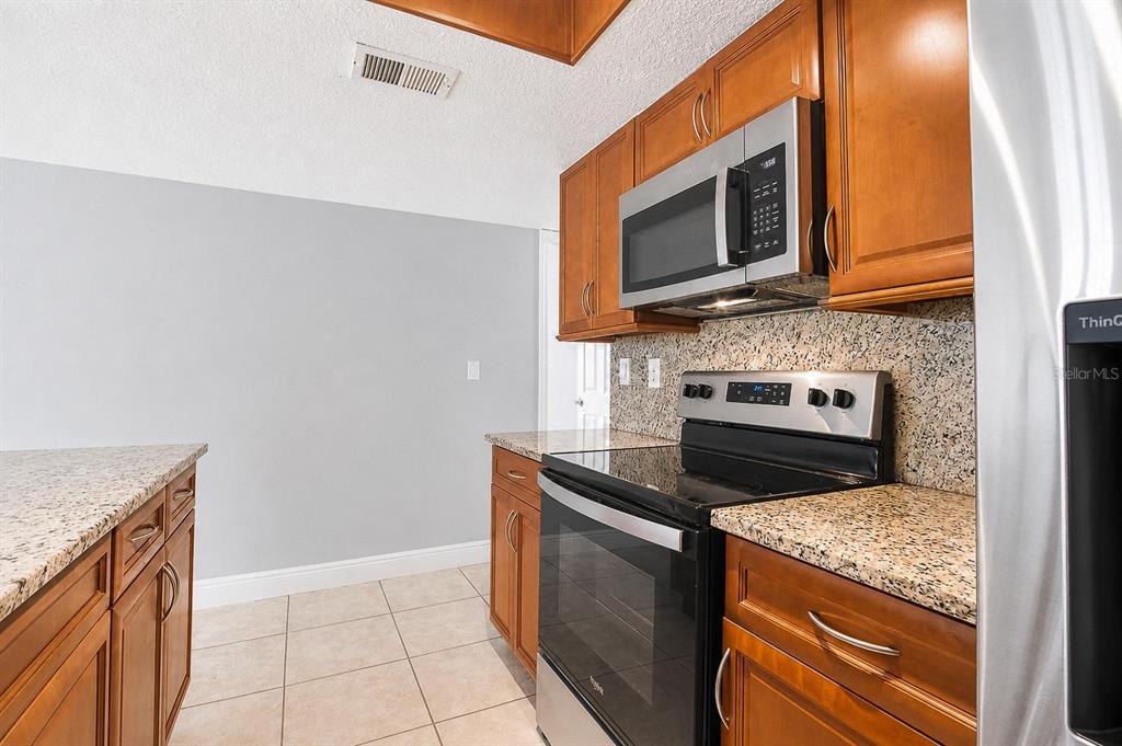 A kitchen features wood cabinets, granite countertops, stainless steel appliances, and light tile flooring — 2739 N POINCIANA BOULEVARD UNIT 79, KISSIMMEE, FL