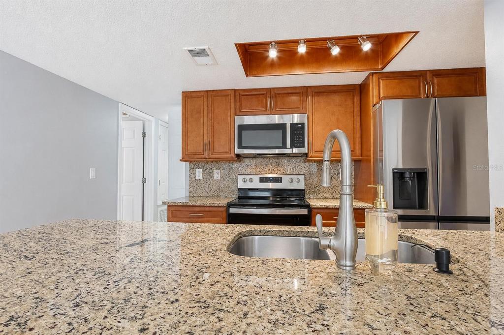 A kitchen features granite countertops, wood cabinets, stainless steel appliances, and a recessed light fixture — 2739 N POINCIANA BOULEVARD UNIT 79, KISSIMMEE, FL