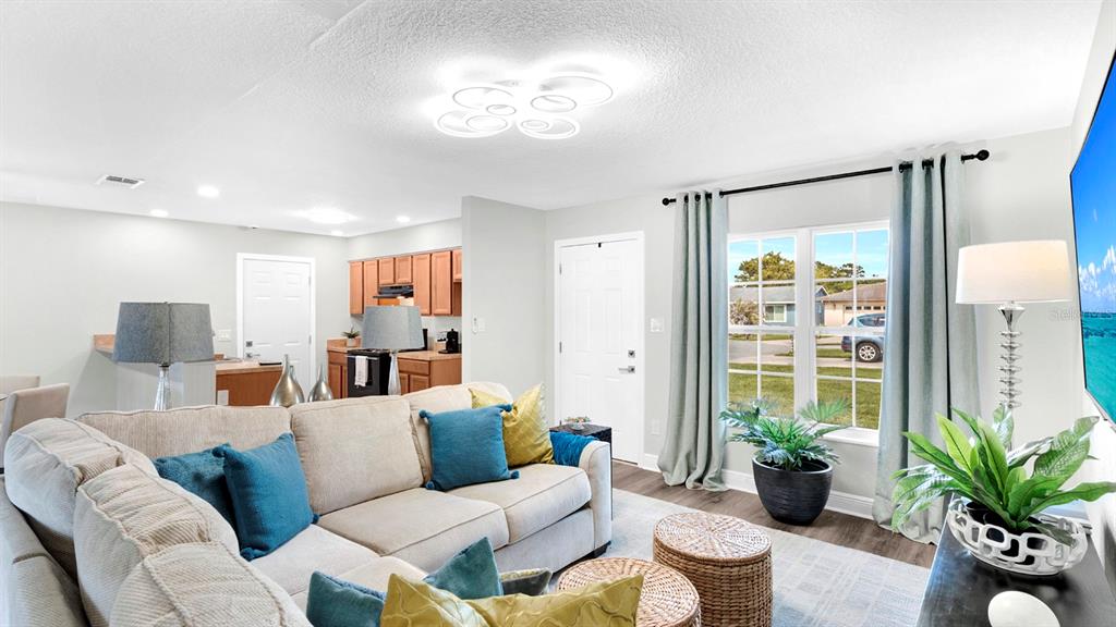 A living room with a beige sofa, blue and gold pillows, and an open kitchen — 10230 GENESEE LANE, ORLANDO, FL