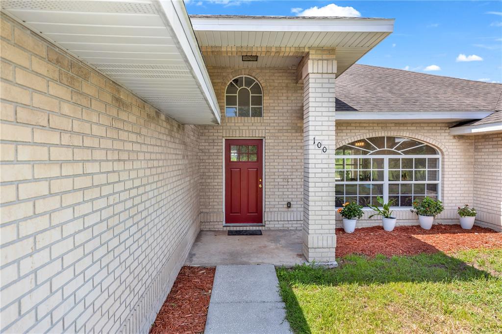 A brick house exterior features a red front door, a concrete walkway, and arched windows — 1005 WHISPRING CREEK WAY, OSTEEN, FL