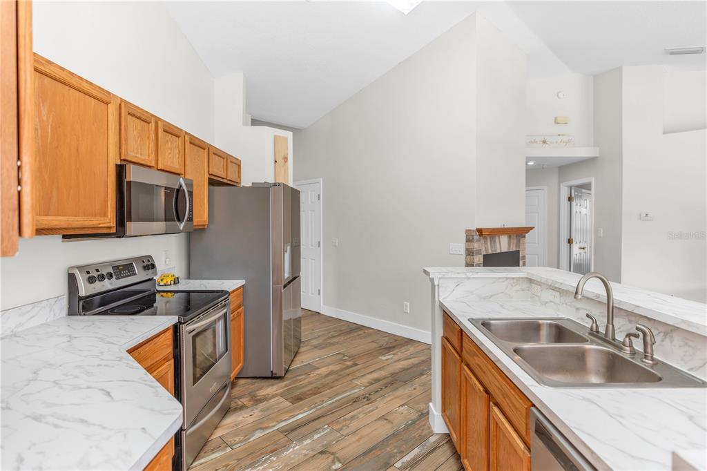 A kitchen with wood cabinets, stainless steel appliances, and white marble-look countertops — 1005 WHISPRING CREEK WAY, OSTEEN, FL