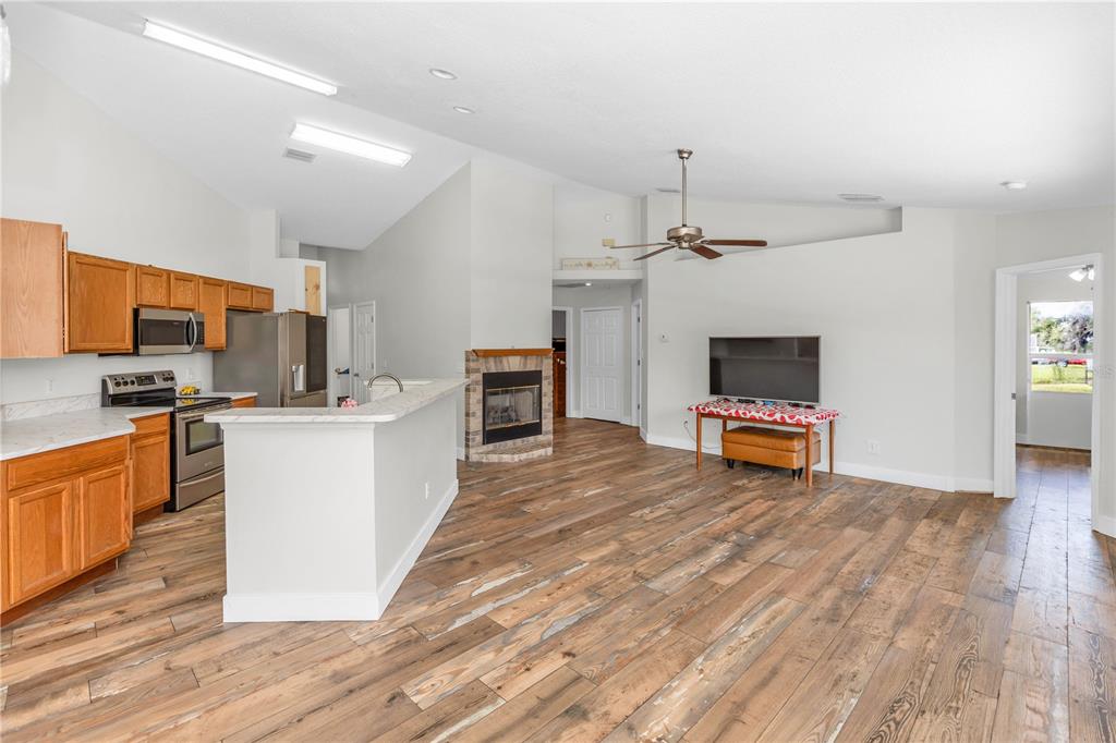 An open-concept living room and kitchen featuring wood-look flooring, a fireplace, and vaulted ceilings — 1005 WHISPRING CREEK WAY, OSTEEN, FL