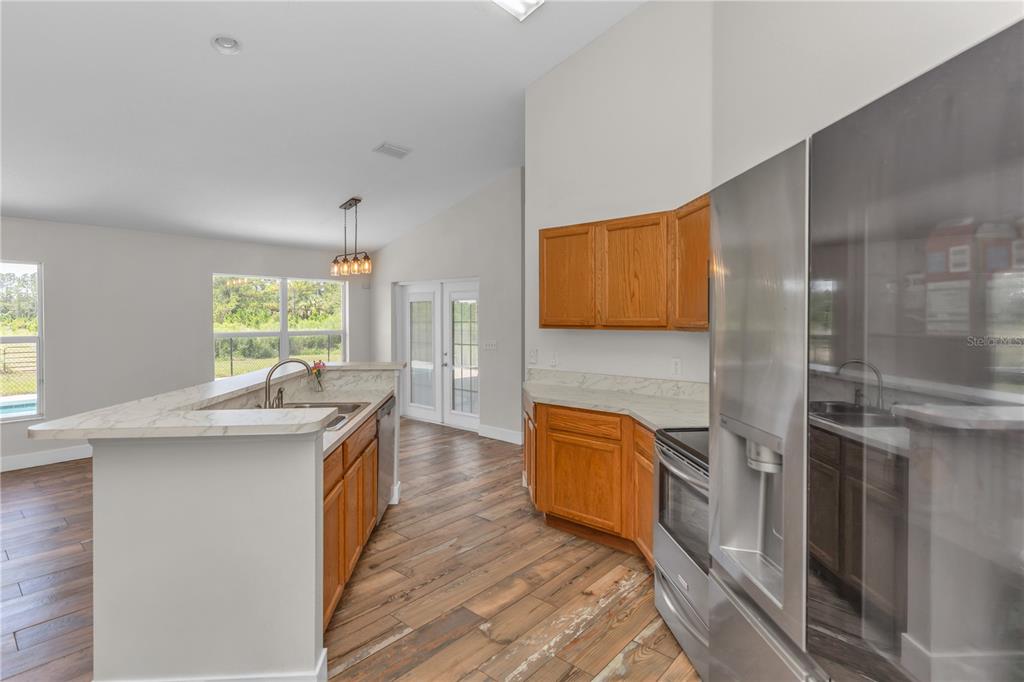 A kitchen with wood cabinets, white countertops, stainless steel appliances, and wood-look tile flooring — 1005 WHISPRING CREEK WAY, OSTEEN, FL