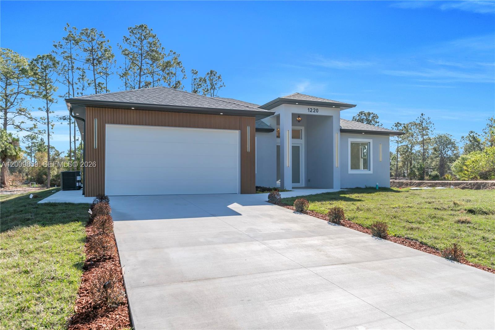 A modern single-story house features a two-car garage with wood-slat accents and a concrete driveway — 1220 Euclid Ave, Lehigh Acres FL 33972, LEHIGH ACRES, FL
