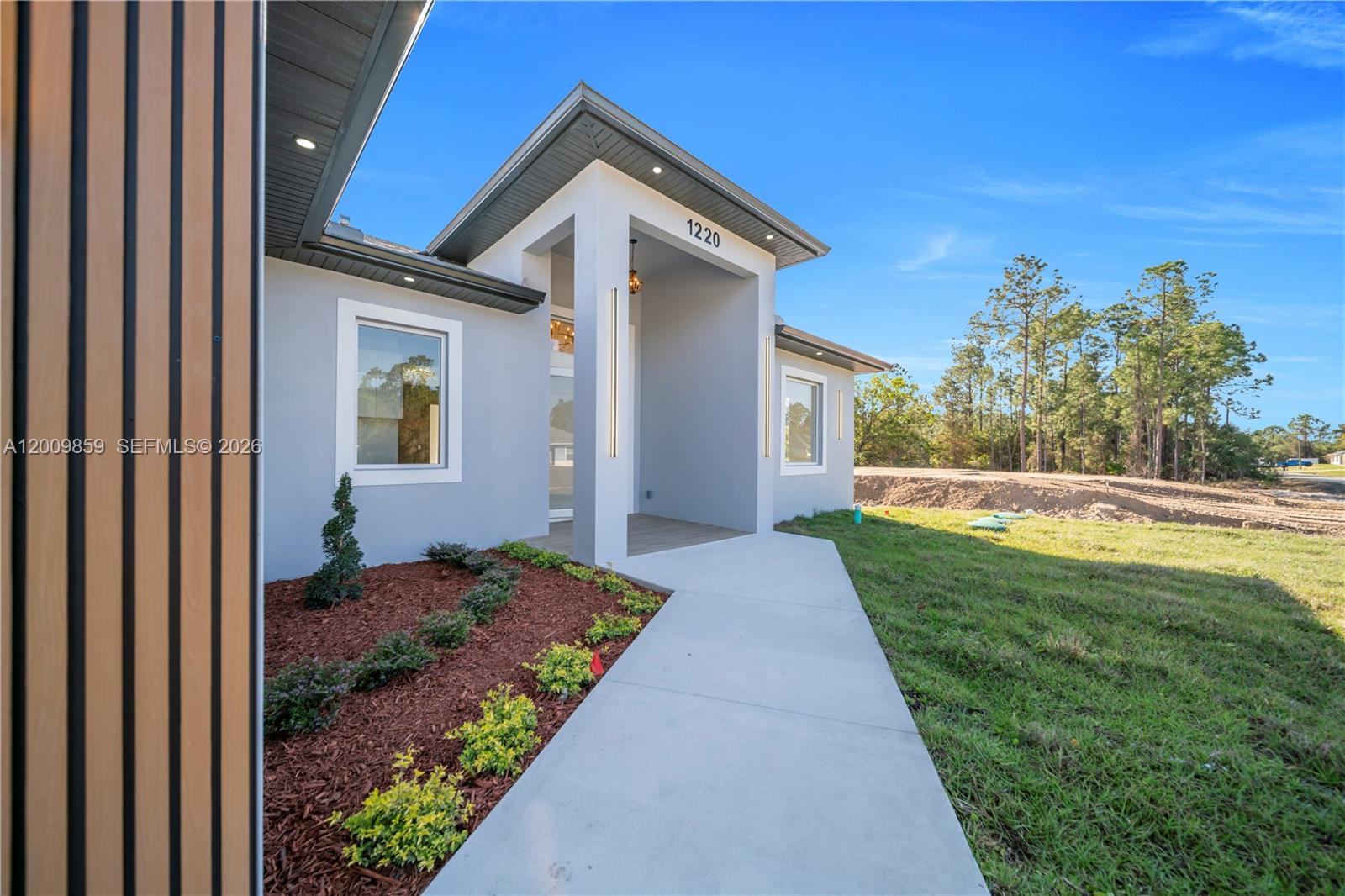A modern house exterior features a gray facade, wood-slat accents, and a concrete walkway — 1220 Euclid Ave, Lehigh Acres FL 33972, LEHIGH ACRES, FL