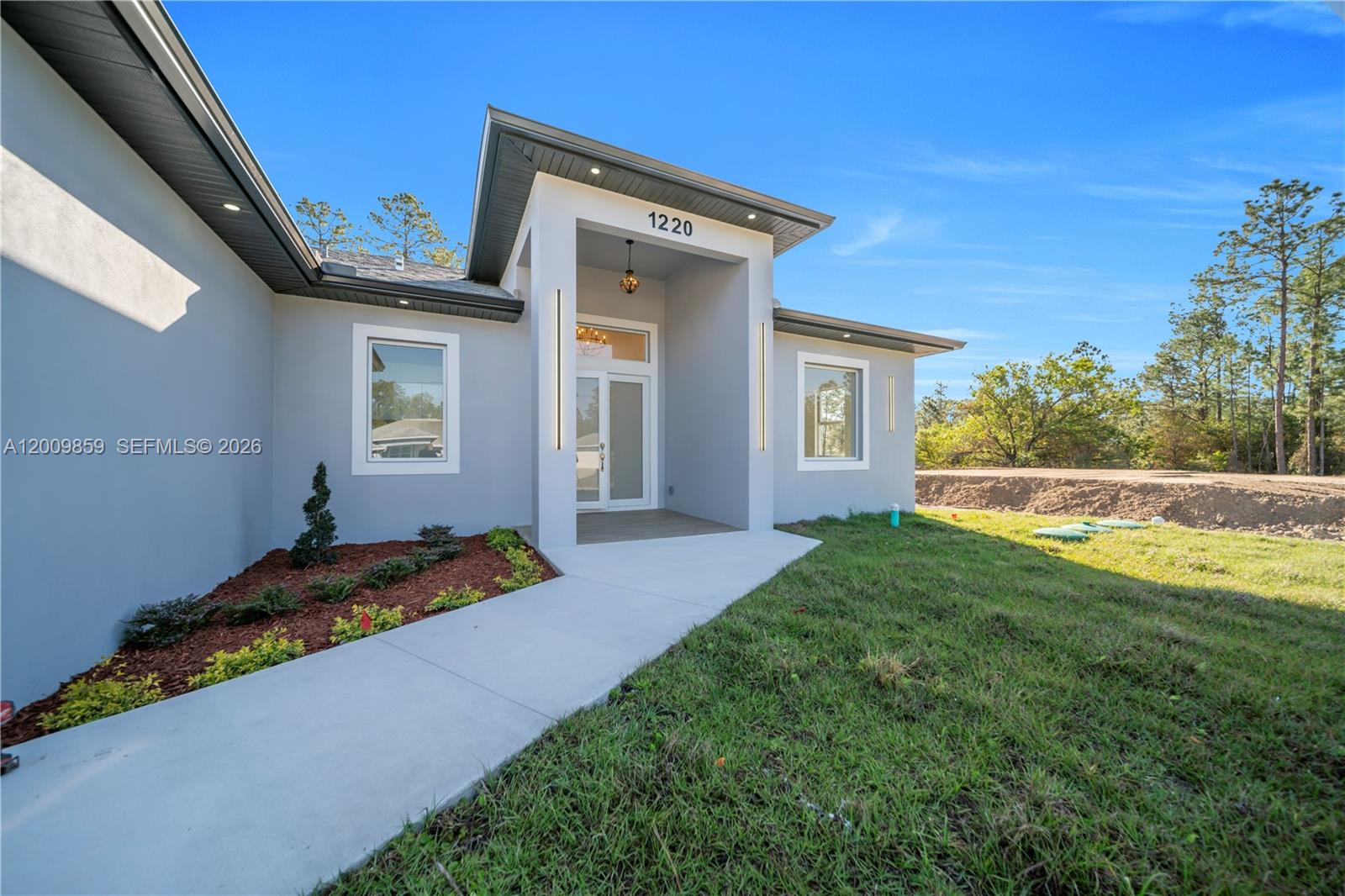 A modern gray house exterior features a covered entryway with a glass front door — 1220 Euclid Ave, Lehigh Acres FL 33972, LEHIGH ACRES, FL