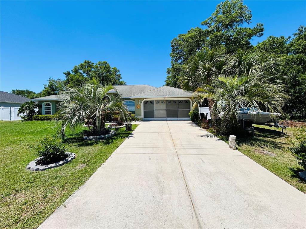 A single-story house with a concrete driveway, palm trees, and a screened-in garage area — 13620 SW 48TH COURT, OCALA, FL