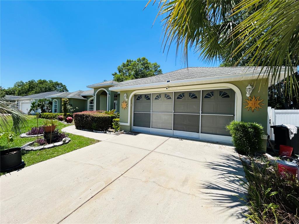 A green house with a two-car garage and a screened-in door faces a concrete driveway — 13620 SW 48TH COURT, OCALA, FL