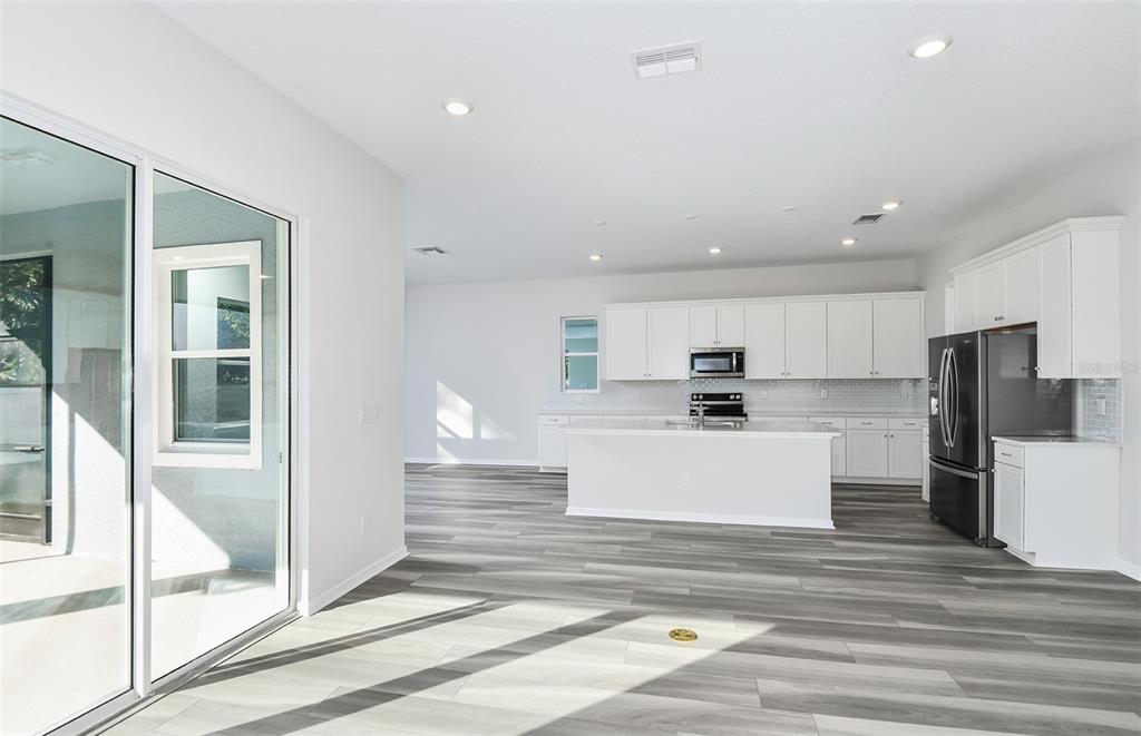 A bright, open-concept kitchen features white cabinetry, a central island, and gray wood-look flooring — 4813 FINLEY DRIVE, DAVENPORT, FL