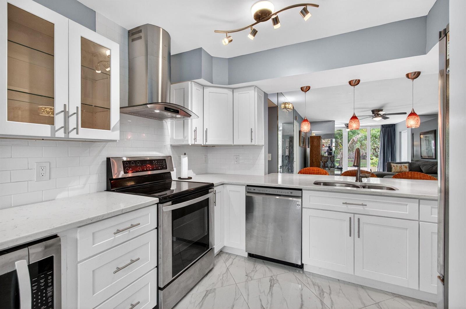 A modern kitchen features white cabinets, stainless steel appliances, quartz countertops, and marble-look tile flooring — 18 Willowbrook Lane # 103, Delray Beach FL 33446, DELRAY BEACH, FL