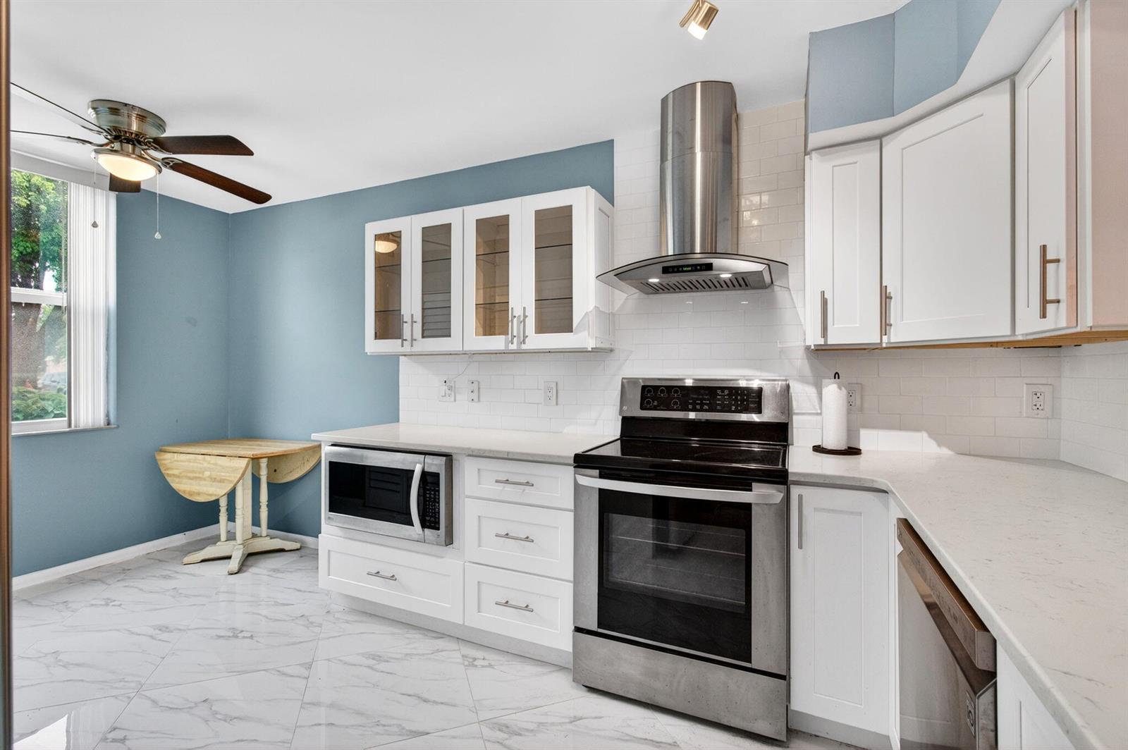 A kitchen features white cabinets, stainless steel appliances, a blue accent wall, and marble-look flooring — 18 Willowbrook Lane # 103, Delray Beach FL 33446, DELRAY BEACH, FL