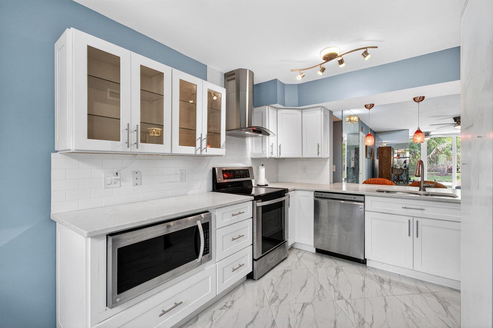 A kitchen with white cabinets, stainless steel appliances, subway tile backsplash, and marble-look tile flooring — 18 Willowbrook Lane # 103, Delray Beach FL 33446, DELRAY BEACH, FL