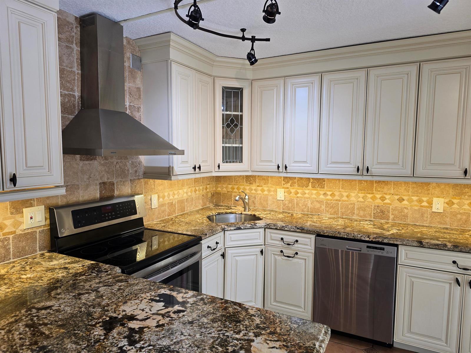 A kitchen features cream-colored cabinets, granite countertops, a stainless steel range, and stone tile backsplashes — 1440 Augusta Circle # 132, Delray Beach FL 33445, DELRAY BEACH, FL
