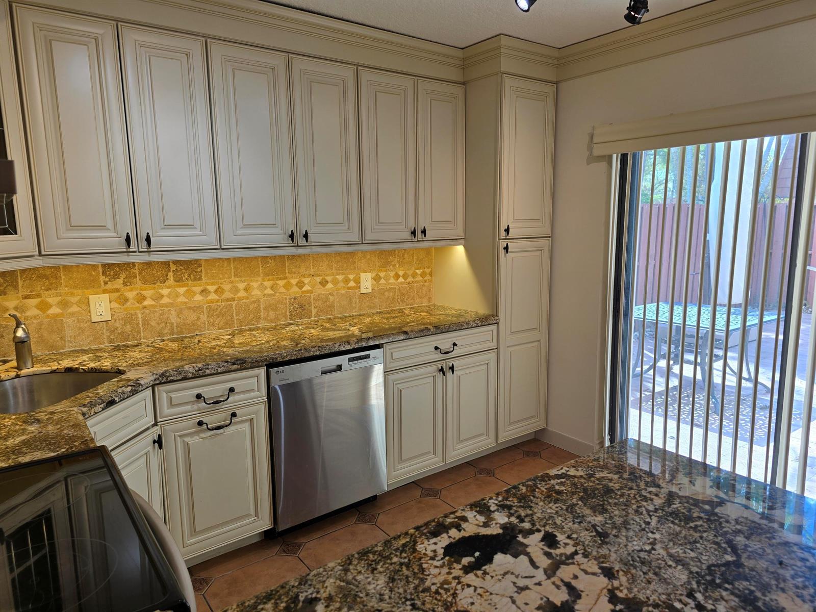 A kitchen features cream-colored cabinets, granite countertops, a tiled backsplash, and a sliding glass door — 1440 Augusta Circle # 132, Delray Beach FL 33445, DELRAY BEACH, FL