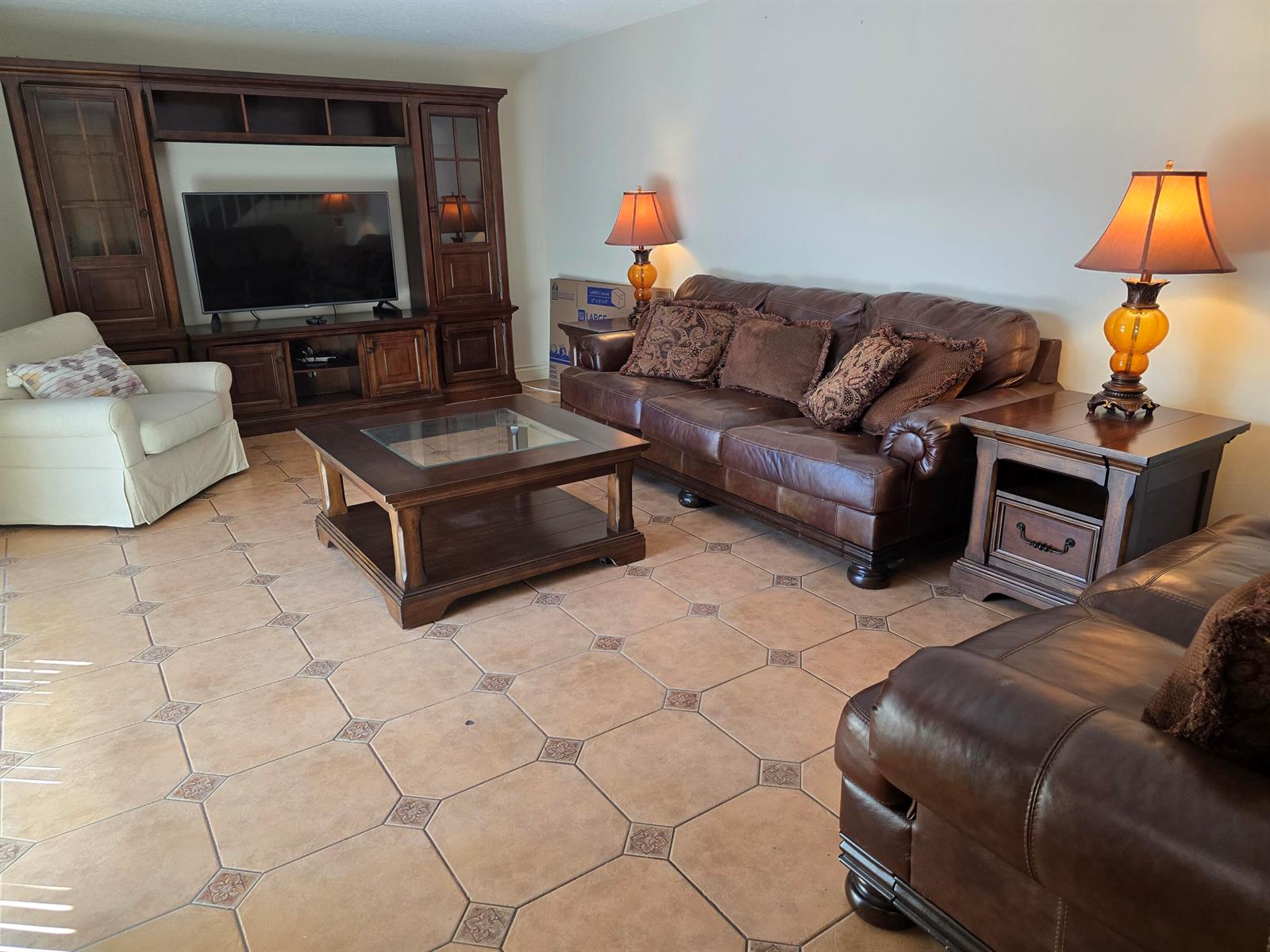 A living room features brown leather sofas, a wooden entertainment center, and tiled flooring — 1440 Augusta Circle # 132, Delray Beach FL 33445, DELRAY BEACH, FL